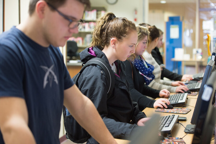 Students standing and working on row of computers