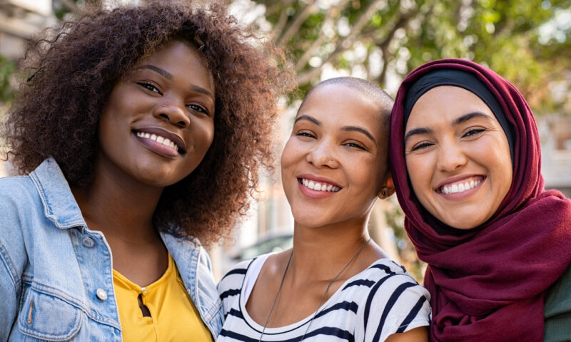 Three diverse female students smiling together.