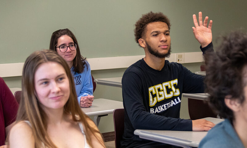 Students sitting in classroom. African American male student raising hand.